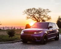 A purple luxury SUV parked on a paved road during sunset, with a scenic background featuring trees and an open field.