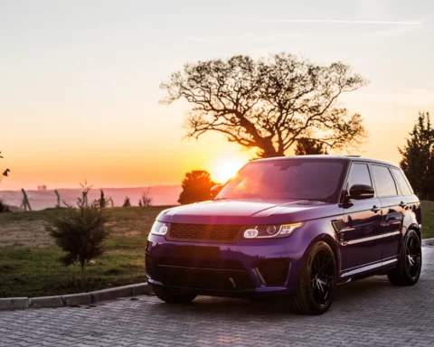 A purple luxury SUV parked on a paved road during sunset, with a scenic background featuring trees and an open field.