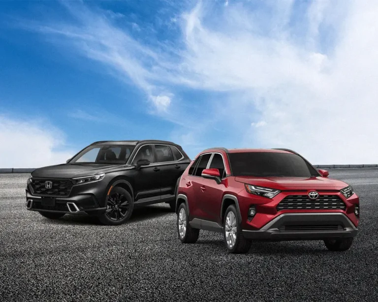 A black 2026 Honda CR-V and a red 2026 Toyota RAV4 parked side by side on an open road under a bright blue sky.