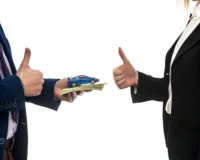 Two people exchange a stack of cash topped with a toy car; both give a thumbs-up, symbolizing a successful car deal and mutual satisfaction in a car purchase transaction