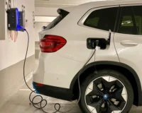 A white BMW electric vehicle is plugged into a wall-mounted charging station in an indoor parking garage, illustrating the process of charging an EV battery.