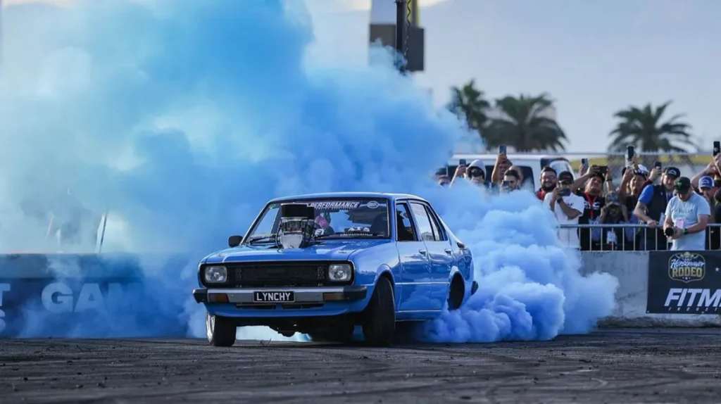 drift cars performing burnouts at SEMA outdoor show with smoke and crowd
